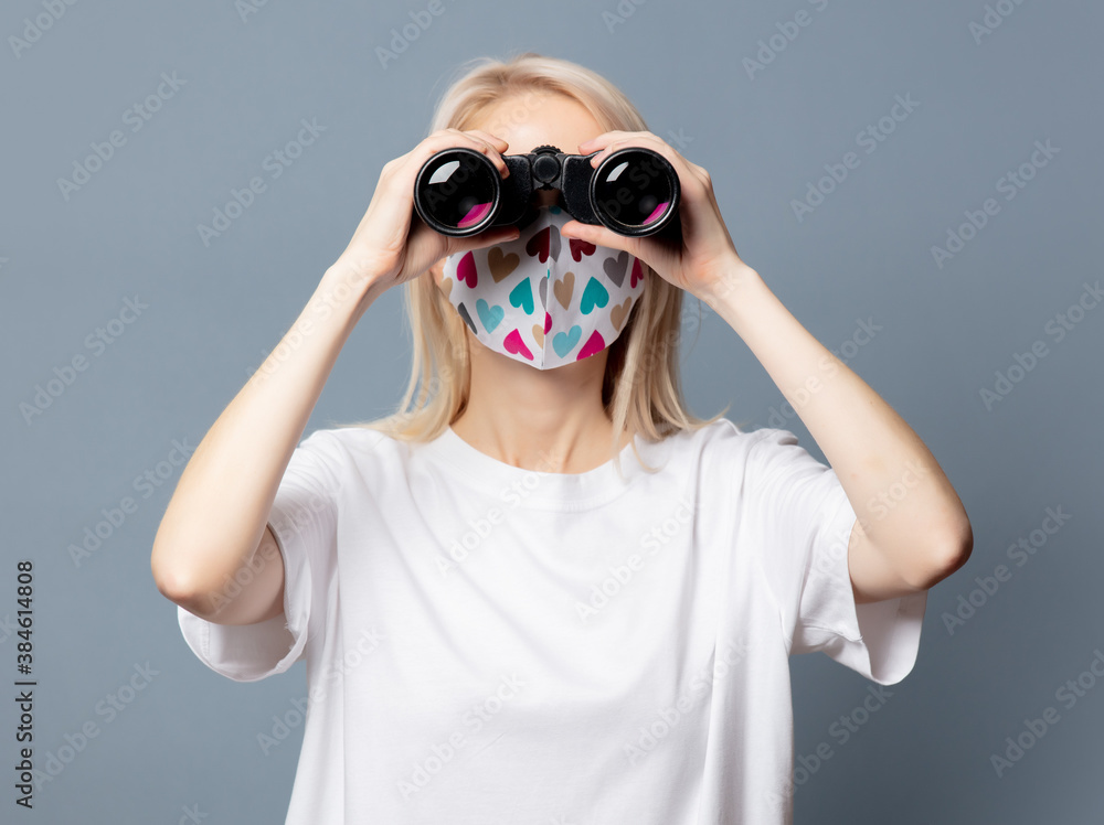Beautiful girl in face mask with binoculars on grey background Beautiful girl in face mask with binoculars on grey background