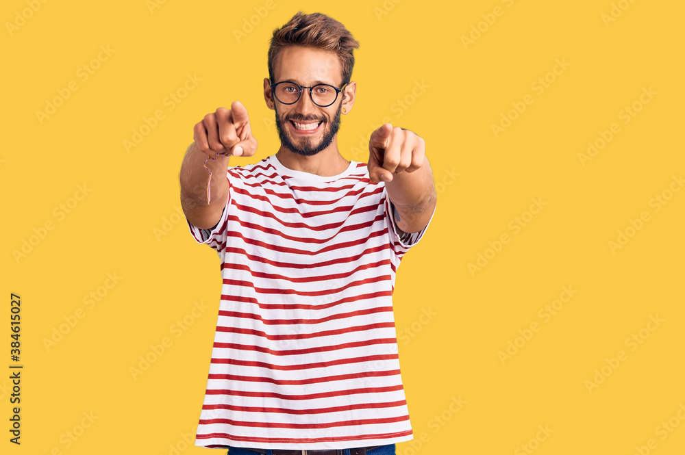 Naklejka premium Handsome blond man with beard wearing casual clothes and glasses pointing to you and the camera with fingers, smiling positive and cheerful