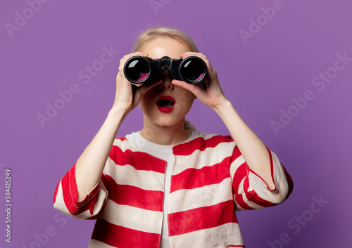 Beautiful blonde in red jacket with binoculars on puprle background