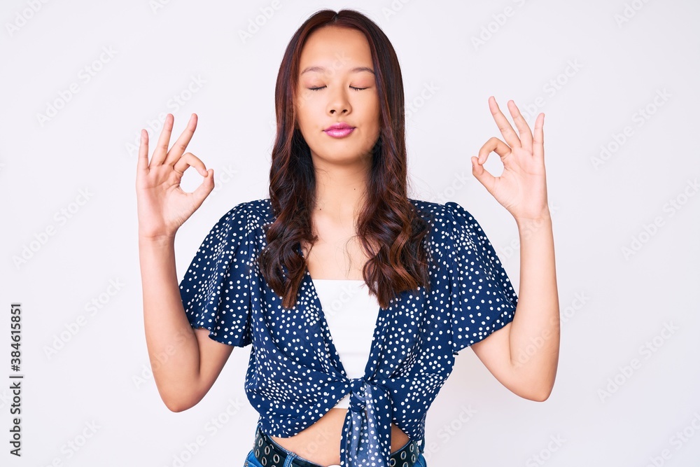 Young beautiful chinese girl wearing casual clothes relax and smiling with eyes closed doing meditation gesture with fingers. yoga concept. Young beautiful chinese girl wearing casual clothes relax and smiling with eyes closed doing meditation gesture with fingers. yoga concept.