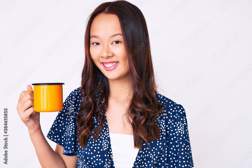 Young beautiful chinese girl holding coffee looking positive and happy standing and smiling with a confident smile showing teeth Young beautiful chinese girl holding coffee looking positive and happy standing and smiling with a confident smile showing teeth