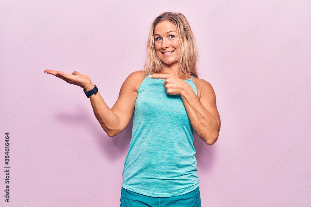 Middle age caucasian blonde woman wearing sports clothes over pink background amazed and smiling to the camera while presenting with hand and pointing with finger. Middle age caucasian blonde woman wearing sports clothes over pink background amazed and smiling to the camera while presenting with hand and pointing with finger.