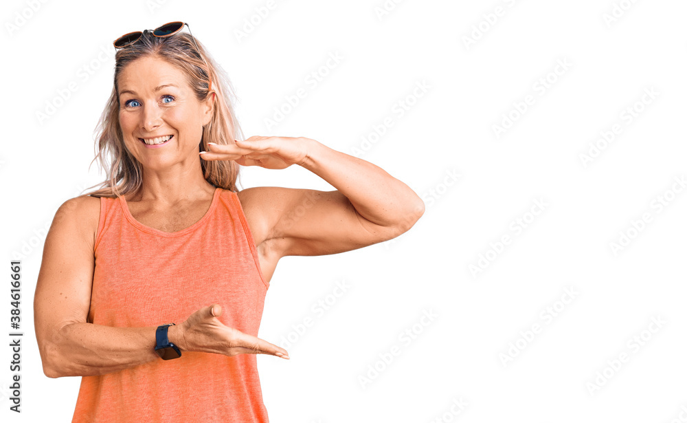 Middle age fit blonde woman wearing casual summer clothes and sunglasses gesturing with hands showing big and large size sign, measure symbol. smiling looking at the camera. measuring concept. Middle age fit blonde woman wearing casual summer clothes and sunglasses gesturing with hands showing big and large size sign, measure symbol. smiling looking at the camera. measuring concept.