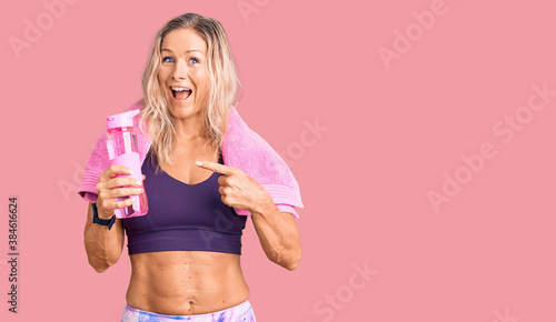Middle age fit blonde woman wearing sportswear wearing towel and holding water bottle smiling happy pointing with hand and finger © Krakenimages.com