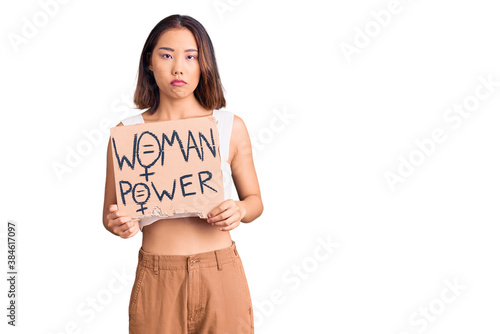 Young beautiful chinese girl holding woman power banner thinking attitude and sober expression looking self confident