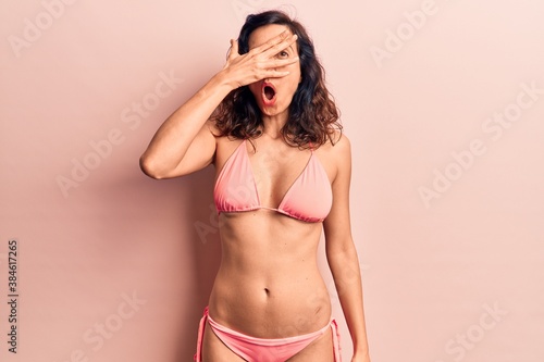 Young beautiful hispanic woman wearing bikini peeking in shock covering face and eyes with hand, looking through fingers afraid © Krakenimages.com