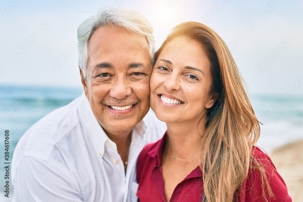 Middle age hispanic couple smiling happy and hugging walking at the beach