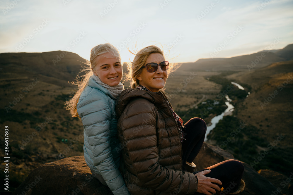 Caucasian mother and daughter bonding while watching beautiful sunset on top of luscious mountain