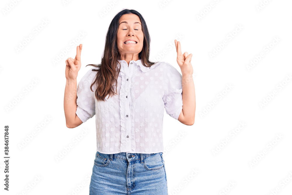 Young beautiful brunette woman wearing casual shirt gesturing finger crossed smiling with hope and eyes closed. luck and superstitious concept. Young beautiful brunette woman wearing casual shirt gesturing finger crossed smiling with hope and eyes closed. luck and superstitious concept.