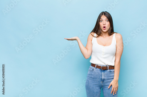 youn pretty woman looking surprised and shocked, with jaw dropped holding an object with an open hand on the side photo