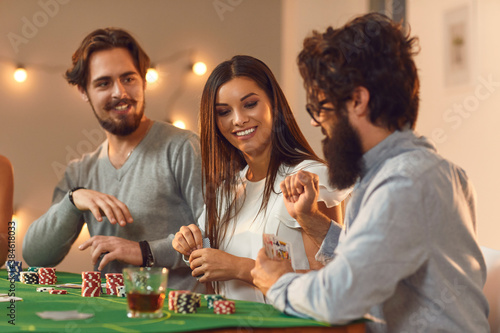 Happy young people playing poker sitting at table with drinks at casino themed party