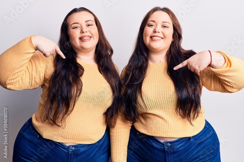 Young plus size twins wearing casual clothes looking confident with smile on face  pointing oneself with fingers proud and happy.