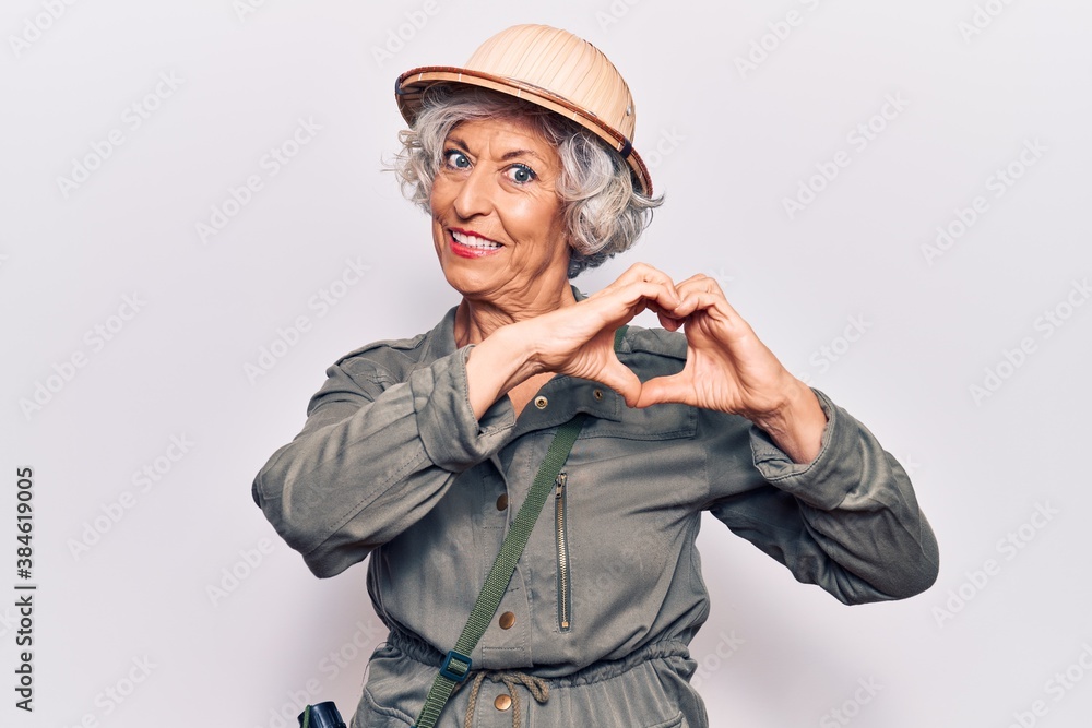 Senior grey-haired woman wearing explorer hat smiling in love showing heart symbol and shape with hands. romantic concept. Senior grey-haired woman wearing explorer hat smiling in love showing heart symbol and shape with hands. romantic concept.