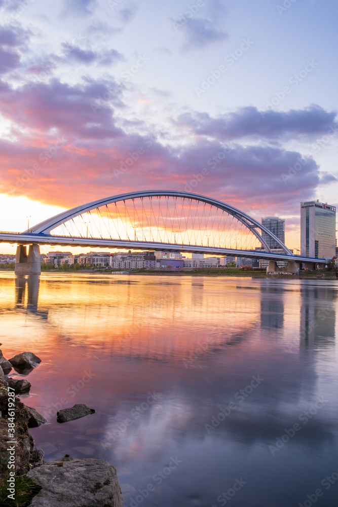 Fototapeta premium Long exposure Apollo bridge over river Danube in Bratislava, Slovakia. Sunset, golden hour, dramatic skies. High rise buildings, travel destination