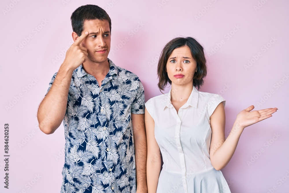 Beautiful couple wearing casual clothes confused and annoyed with open palm showing copy space and pointing finger to forehead. think about it. Beautiful couple wearing casual clothes confused and annoyed with open palm showing copy space and pointing finger to forehead. think about it.
