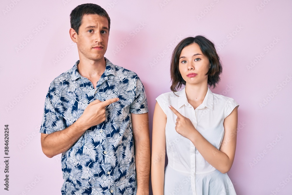 Beautiful couple wearing casual clothes pointing with hand finger to the side showing advertisement, serious and calm face Beautiful couple wearing casual clothes pointing with hand finger to the side showing advertisement, serious and calm face