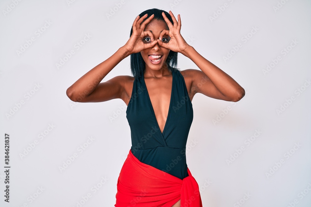 Young african american woman wearing swimsuit doing ok gesture like binoculars sticking tongue out, eyes looking through fingers. crazy expression. Young african american woman wearing swimsuit doing ok gesture like binoculars sticking tongue out, eyes looking through fingers. crazy expression.