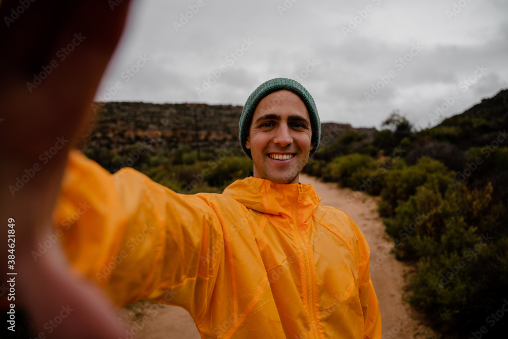 Attractive young male athlete smiling while taking photo of self on run on gravel mountain path in cloudy weather with bushes Attractive young male athlete smiling while taking photo of self on run on gravel mountain path in cloudy weather with bushes