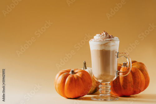 Spice pumpkin latte in glass with pumpkins on yellow background