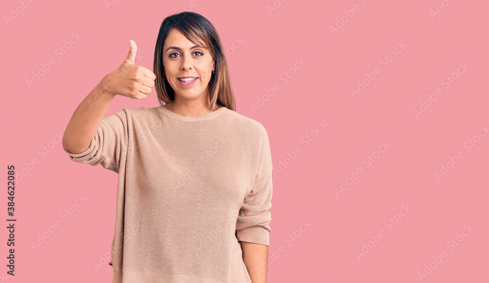 Young beautiful woman wearing casual sweater smiling happy and positive, thumb up doing excellent and approval sign Young beautiful woman wearing casual sweater smiling happy and positive, thumb up doing excellent and approval sign