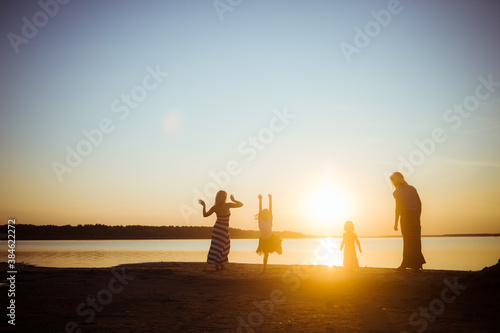 Silhouettes of children and their mothers jumping and having fun on the beach in sunset light. Good mood and pastime among the younger and older generation.