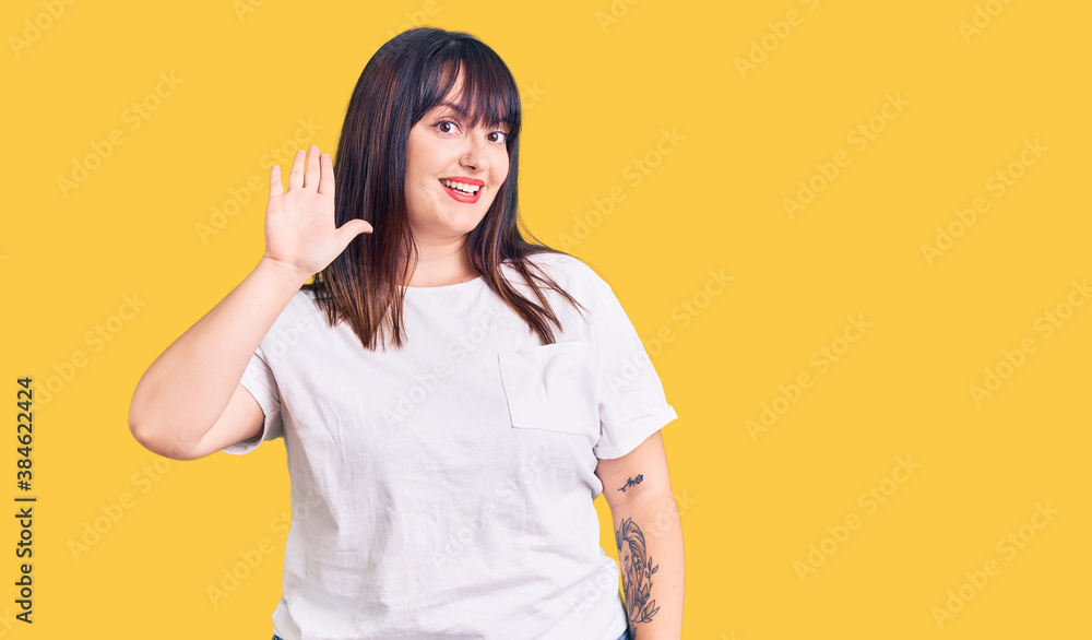 Young plus size woman wearing casual clothes waiving saying hello happy and smiling, friendly welcome gesture Young plus size woman wearing casual clothes waiving saying hello happy and smiling, friendly welcome gesture