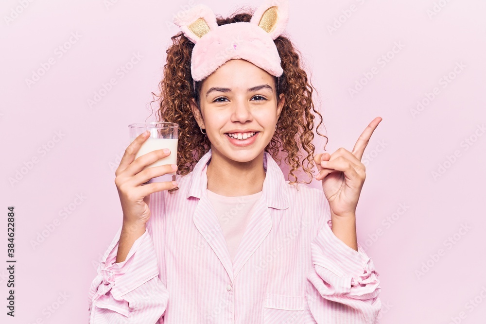 Beautiful kid girl with curly hair wearing sleep mask and pajama holding milk smiling happy pointing with hand and finger to the side Beautiful kid girl with curly hair wearing sleep mask and pajama holding milk smiling happy pointing with hand and finger to the side
