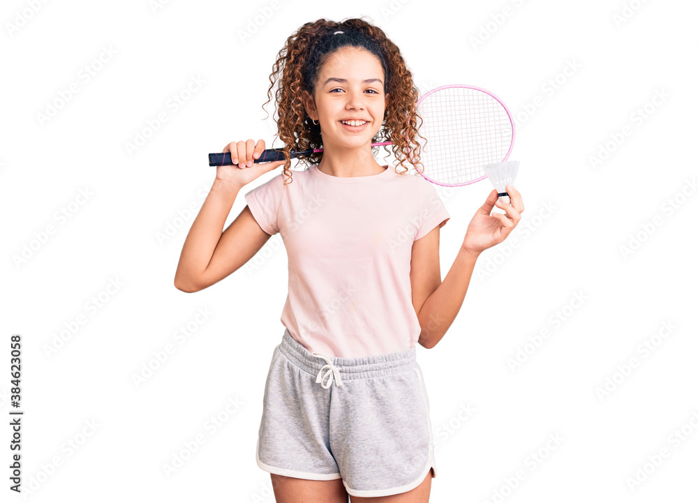 Beautiful kid girl with curly hair holding badminton racket and shuttlecock looking positive and happy standing and smiling with a confident smile showing teeth Beautiful kid girl with curly hair holding badminton racket and shuttlecock looking positive and happy standing and smiling with a confident smile showing teeth