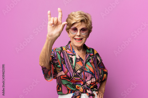 old pretty woman feeling happy, fun, confident, positive and rebellious, making rock or heavy metal sign with hand photo