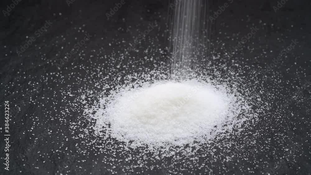 White sugar falling into a black stone board White sugar falling into a black stone board