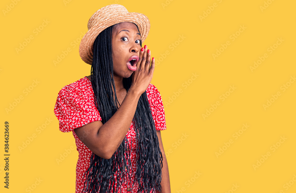 Young african american woman wearing summer hat hand on mouth telling secret rumor, whispering malicious talk conversation Young african american woman wearing summer hat hand on mouth telling secret rumor, whispering malicious talk conversation