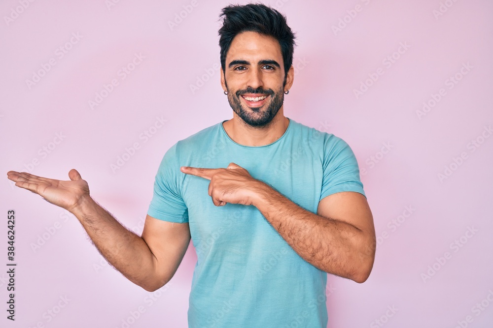 Fototapeta premium Handsome hispanic man with beard wearing casual clothes amazed and smiling to the camera while presenting with hand and pointing with finger.