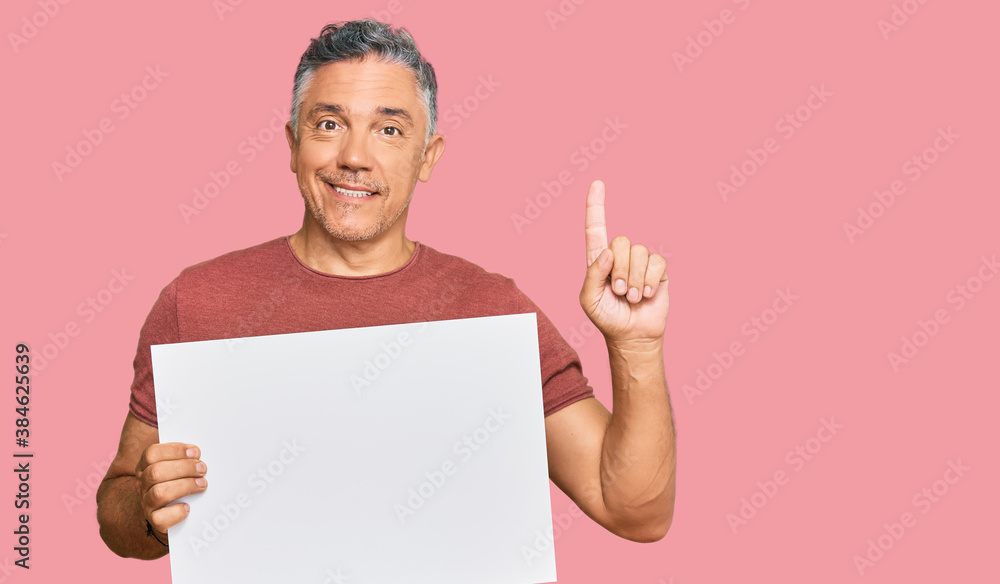 Handsome middle age man holding blank empty banner surprised with an idea or question pointing finger with happy face, number one Handsome middle age man holding blank empty banner surprised with an idea or question pointing finger with happy face, number one