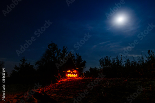 Carved halloween pumpkin jack-o-lantern wearing witch hat with burning candles glows in a darkness. Spooky landscape