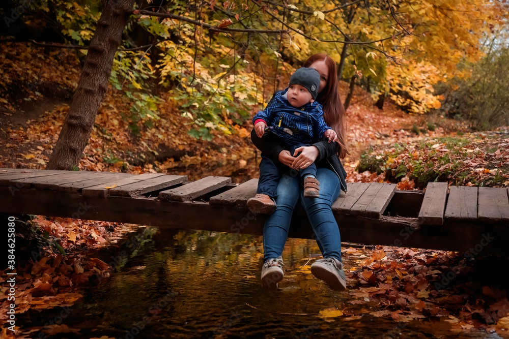 Mother and son in the autumn Park. A woman with a child in her arms, sitting on a wooden bridge.