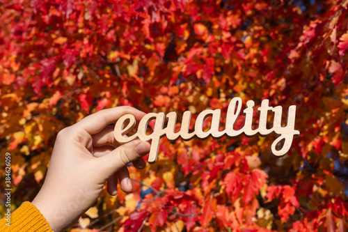 The word "equality" in a woman's hand against the background of autumn foliage