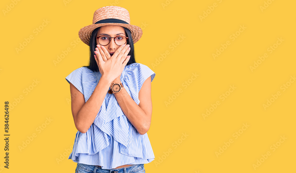Young beautiful latin girl wearing summer hat and glasses shocked covering mouth with hands for mistake. secret concept. Young beautiful latin girl wearing summer hat and glasses shocked covering mouth with hands for mistake. secret concept.