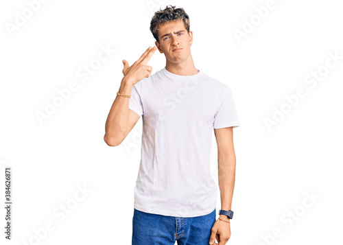 Canvas Print Young handsome man wearing casual white tshirt shooting and killing oneself pointing hand and fingers to head like gun, suicide gesture