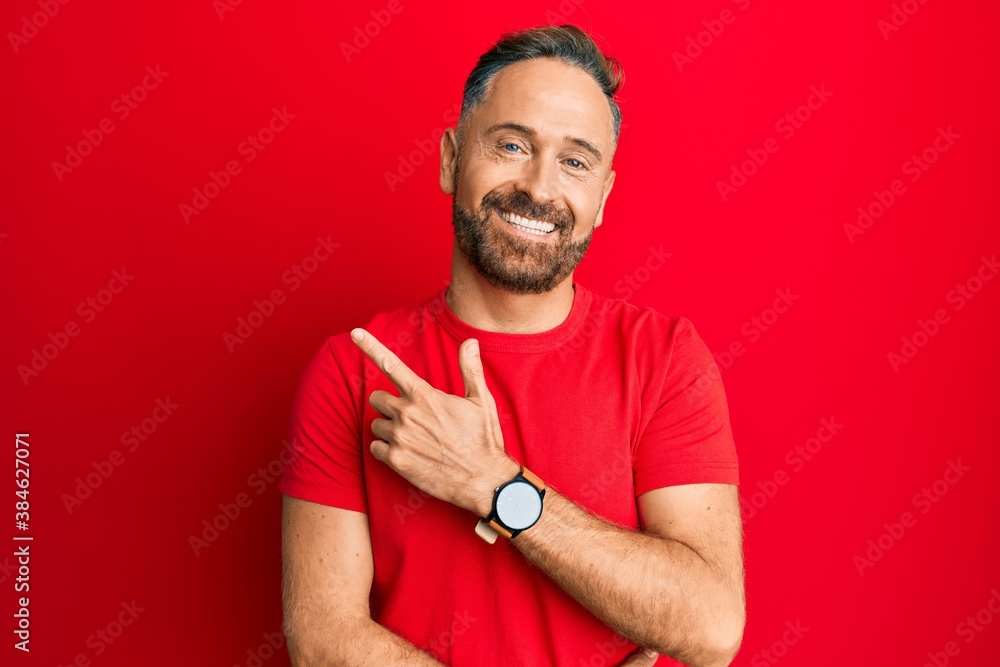 Fototapeta premium Handsome middle age man wearing casual red tshirt smiling cheerful pointing with hand and finger up to the side