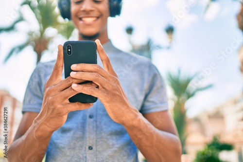 Young african american man smiling happy using smartphone and headphones at the city.