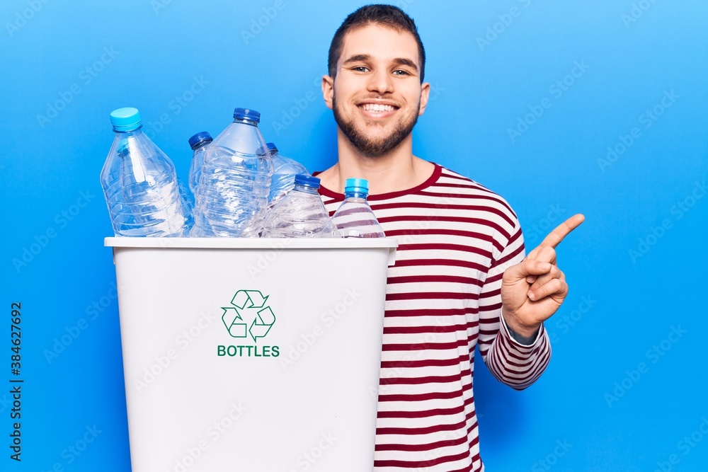 Young handsome man recycling plastic bottles smiling happy pointing with hand and finger to the side Young handsome man recycling plastic bottles smiling happy pointing with hand and finger to the side