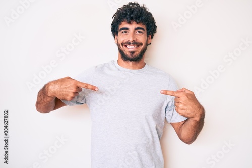 Tableau sur toile Handsome young man with curly hair and bear wearing casual tshirt looking confident with smile on face, pointing oneself with fingers proud and happy