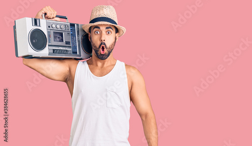 Young hispanic man holding boombox, listening to music scared and amazed with open mouth for surprise, disbelief face