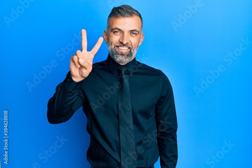 Middle age handsome man wearing business shirt and tie showing and pointing up with fingers number two while smiling confident and happy.