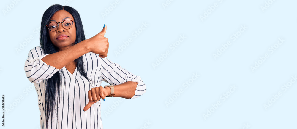 Obraz premium Young african american woman wearing casual clothes and glasses doing thumbs up and down, disagreement and agreement expression. crazy conflict