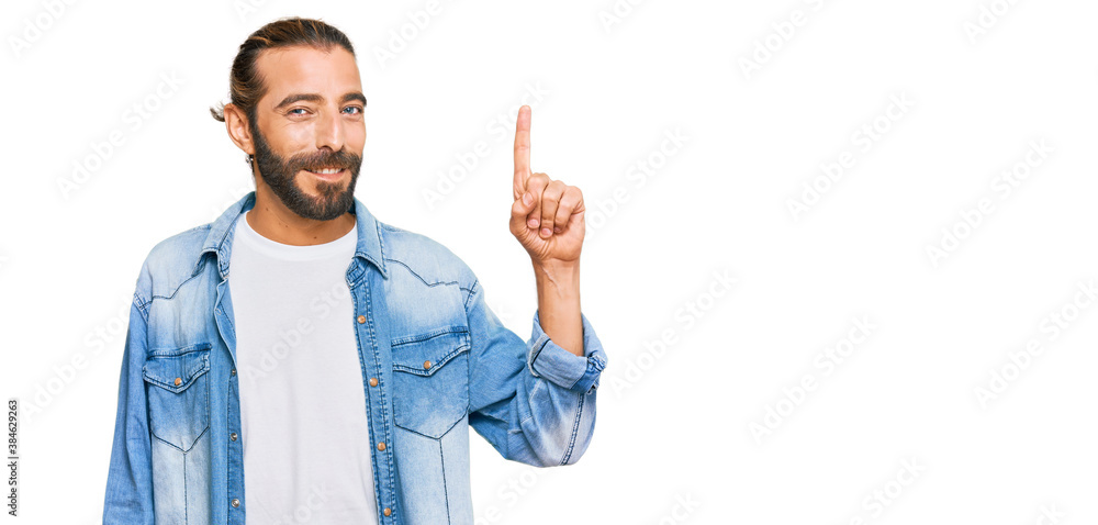 Attractive man with long hair and beard wearing casual denim jacket showing and pointing up with finger number one while smiling confident and happy. Attractive man with long hair and beard wearing casual denim jacket showing and pointing up with finger number one while smiling confident and happy.
