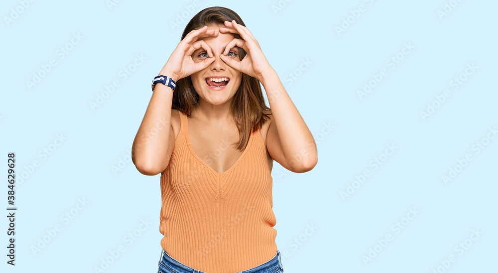 Young caucasian woman wearing casual clothes doing ok gesture like binoculars sticking tongue out, eyes looking through fingers. crazy expression.