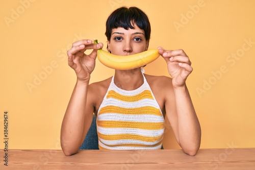 Brunette teenager girl holding banana like funny smile relaxed with serious expression on face. simple and natural looking at the camera.