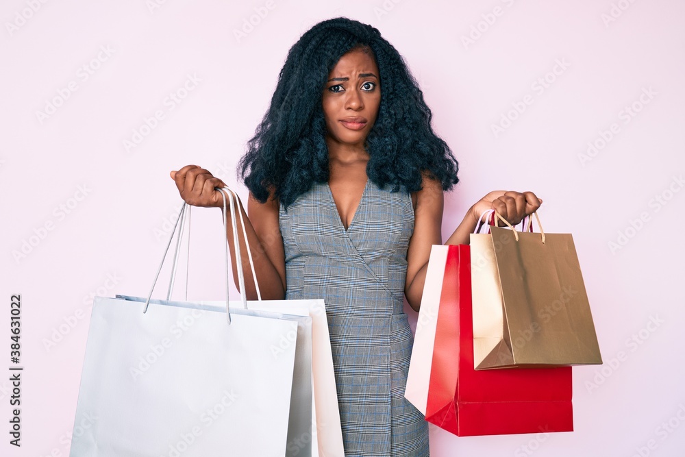 Young african american woman holding shopping bags skeptic and nervous, frowning upset because of problem. negative person. Young african american woman holding shopping bags skeptic and nervous, frowning upset because of problem. negative person.