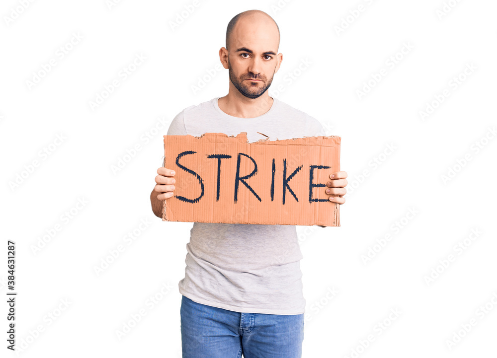 Young handsome man holding strike banner thinking attitude and sober expression looking self confident Young handsome man holding strike banner thinking attitude and sober expression looking self confident
